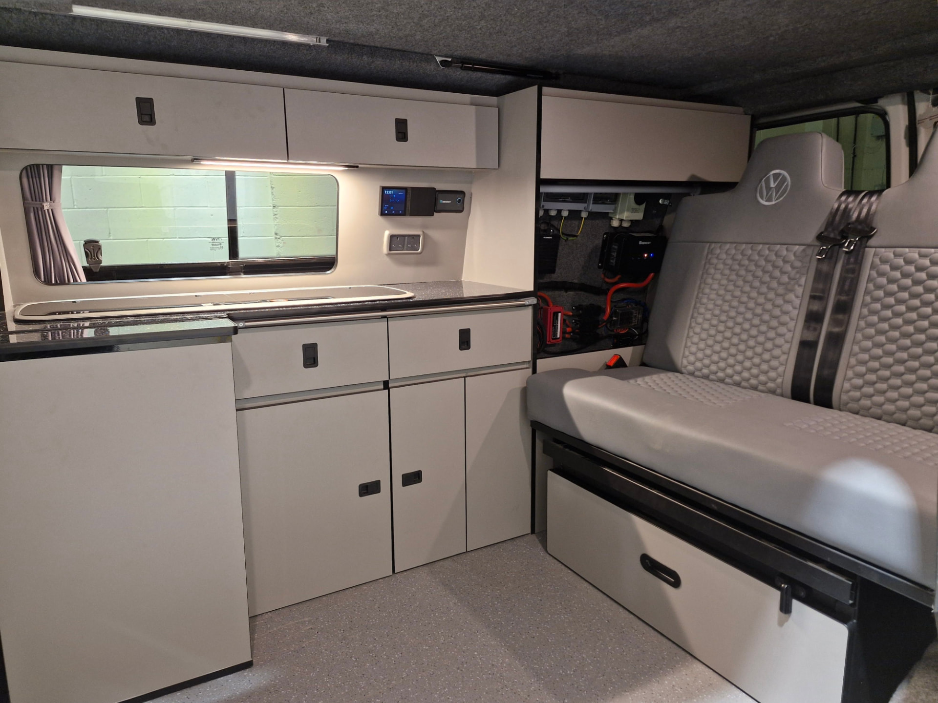 Full-width campervan furniture run with light grey units, overhead lockers, worktop sink and electrical control panel