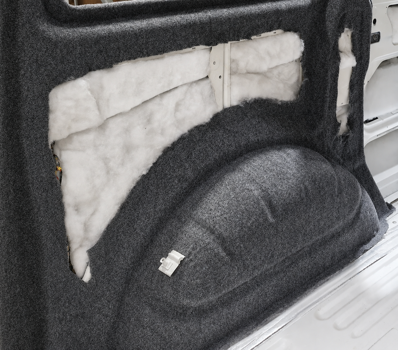 Thermo fleece insulation packed behind grey carpet lining on a van side panel