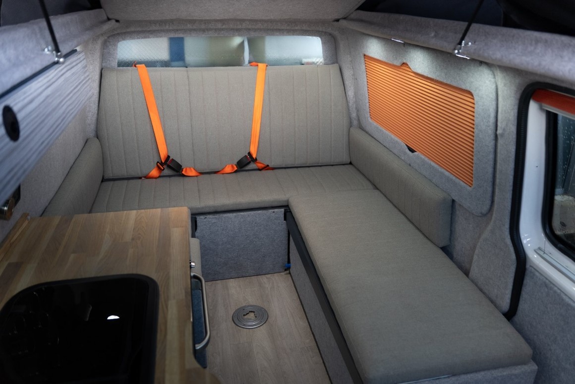 Finished campervan interior with a U-shaped rear lounge and belted travel seating