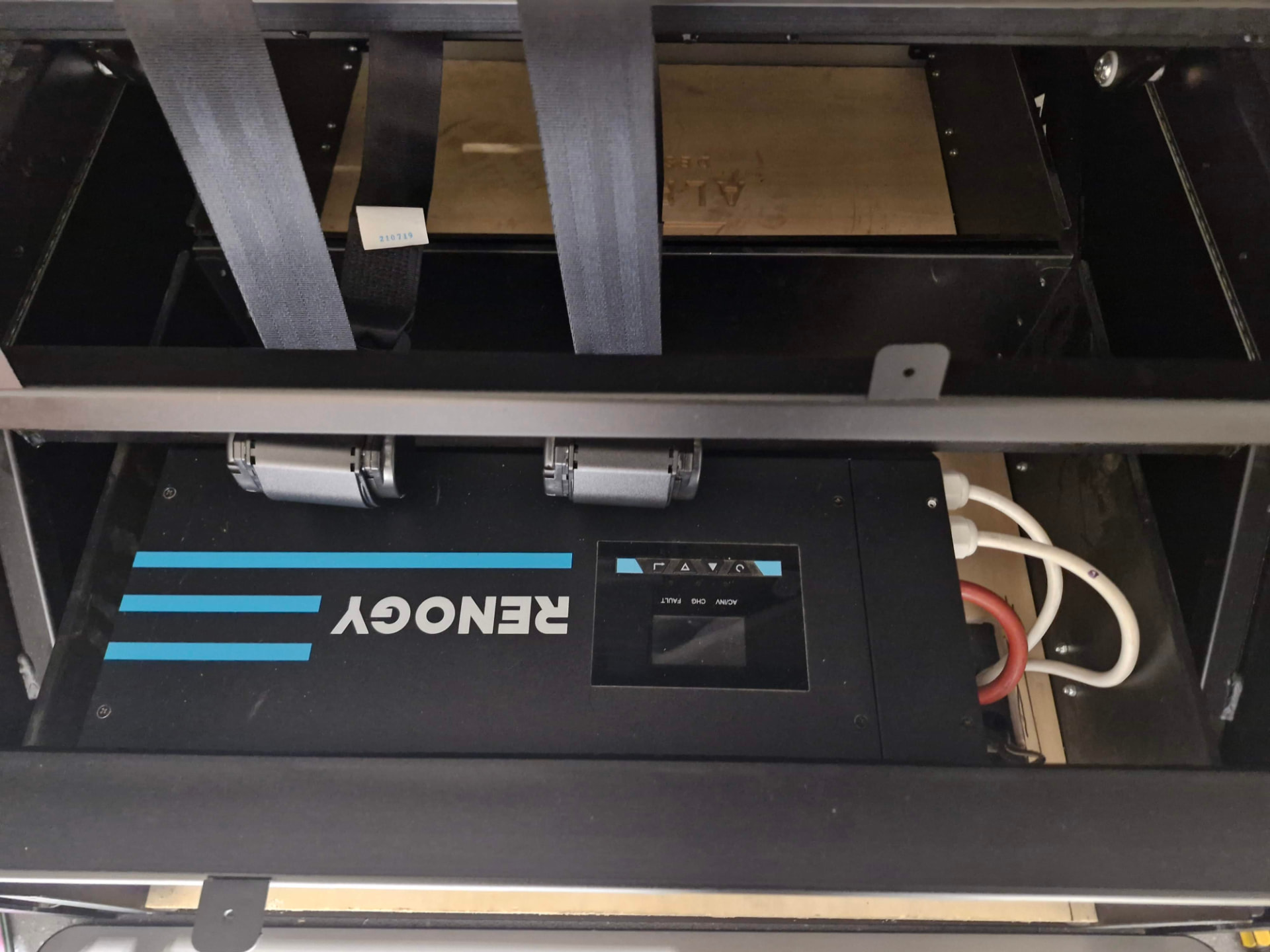 Inverter-charger mounted under a rock and roll bed frame in a campervan