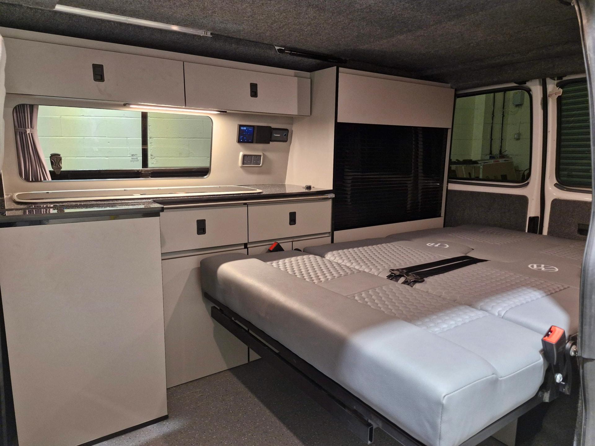 Clean campervan interior with a folded bed and fitted kitchen